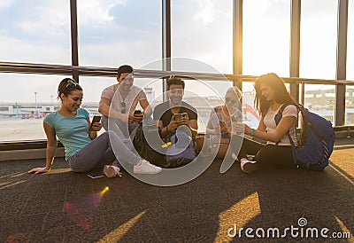 Young People Group Sitting On Floor Airport Lounge Waiting Departure Use Cell Smart Phone Chatting Mix Race Friends Stock Photo