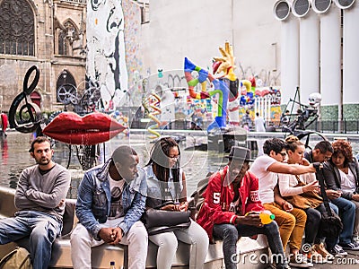 Young people lounge and talk on the wall surrounding the Fontaine de Stravinsky in central Paris, France Editorial Stock Photo