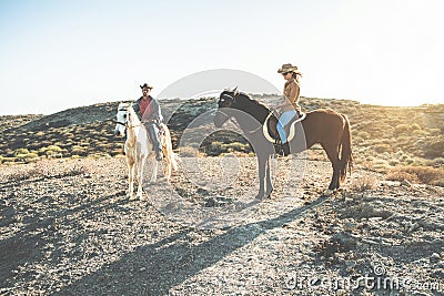 Young people riding horses doing excursion at sunset - Wild couple having fun in equestrian tour - Training, culture, passion, Stock Photo