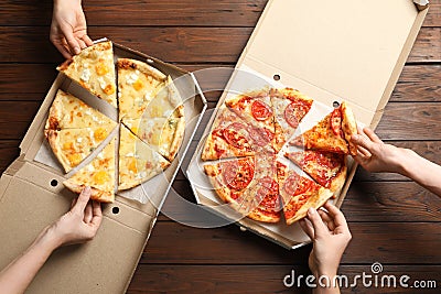 Young people taking slices of hot cheese pizzas from cardboard boxes at table, top view. Stock Photo