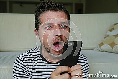 Young perplexed and shocked man using mobile phone looking internet social media or checking news in surprised and crazy disbelief Stock Photo