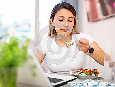 Peruvian housewoman eating salad and watching movie on laptop Stock Photo