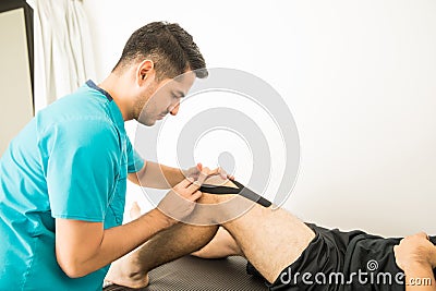 Physiotherapy Professional Applying KT Tape On Athlete`s Knee Stock Photo