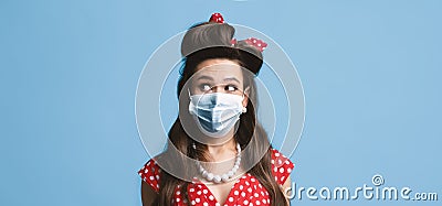 Young pinup lady in retro dress wearing face mask against covid-19, looking aside at blank space on blue background Stock Photo