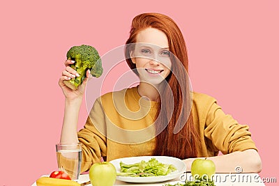 Pretty redhead caucasian woman sitting at table with healthy food and broccoli Stock Photo