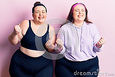 Young plus size twins wearing sportswear very happy and excited doing winner gesture with arms raised, smiling and screaming for Stock Photo