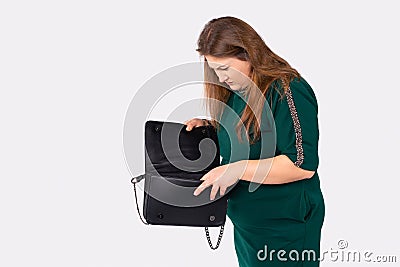 Young plus size woman searches in elegant black bag. Stylish plump blonde in green dress, looking for a wallet, keys Stock Photo