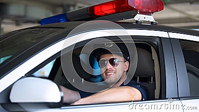 Young policeman in sunglasses sitting in car smiling into camera, important job Stock Photo