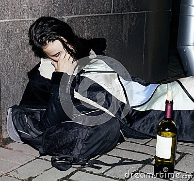 young poor ttenage girl sitting at dirty wall on floor with bott Stock Photo
