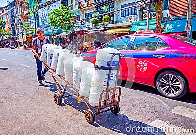 Young porter carying large packs of ice along the road at Pak Khlong Talat Flower Market in Bangkok, Thailand Editorial Stock Photo