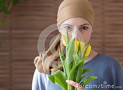 Young positive adult female cancer patient holding bouquet of yellow tulips, smiling and looking at camera. Stock Photo