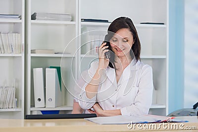 Young practitioner doctor working at the clinic reception desk, she is answering phone calls and scheduling appointments Stock Photo