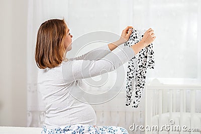 A young pregnant woman shows off her tummy and inflates a bubble of gum. White window in the background. Conception of Stock Photo