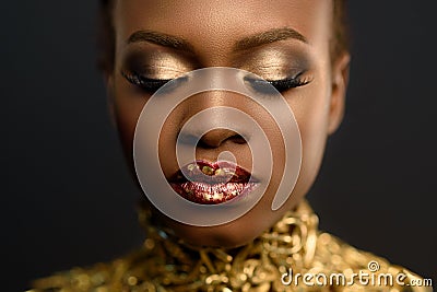 Young pretty african woman, with hair gathered in hairstyle and sensitive gold make-up, posing on black background, in studio, clo Stock Photo