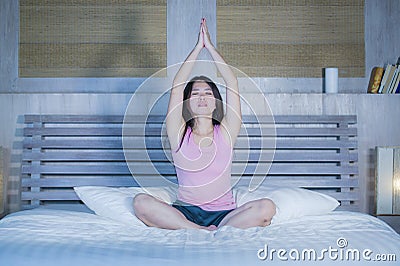 Young pretty Asian Chinese woman 20s or 30s relaxing at home bedroom sitting on bed in lotus yoga position in meditation and relax Stock Photo