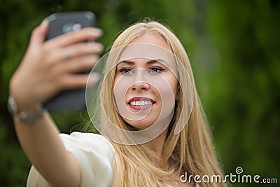 Young beautiful blonde girl in a dress makes a selfie on the street in summer. Stock Photo