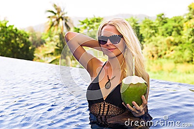 Young pretty blonde woman in swimming pool with coconut coctail Stock Photo