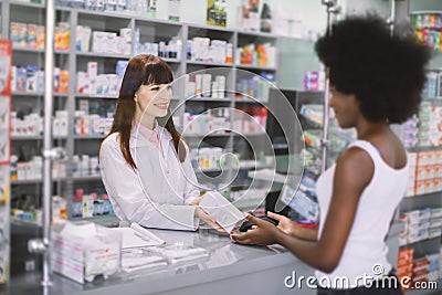 Young pretty Caucasian woman pharmacist helping a female African customer, dispensing her prescription medicine with a Stock Photo