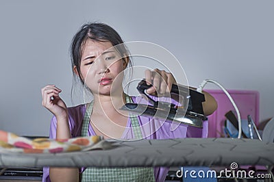 Young pretty frustrated and stressed Asian Chinese woman with iron working at home kitchen ironing clothes desperate and overwhelm Stock Photo