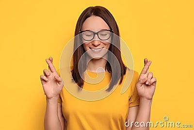 Young pretty girl with eyeglasses and crossed fingers posing on yellow background with closed eyes Stock Photo