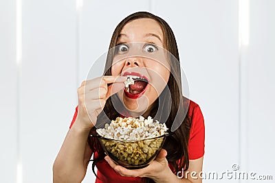 Young pretty girl with opened mouth and wide eyes holds glass bowl with popcorn Stock Photo