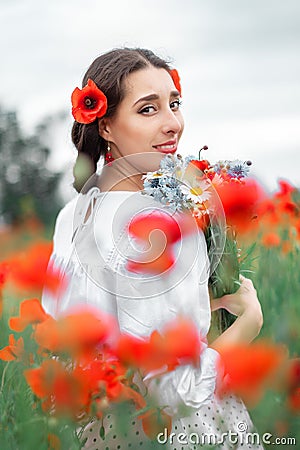 Young pretty girl Slavic or Ukrainian posing in folk dress on a flowering poppy field. Stock Photo