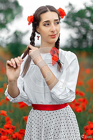 Young pretty girl Slavic or Ukrainian posing in folk dress on a flowering poppy field. Female weaving braid. Stock Photo