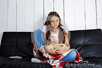 Young pretty girl watching tv, sitting on sofa at home. Stock Photo