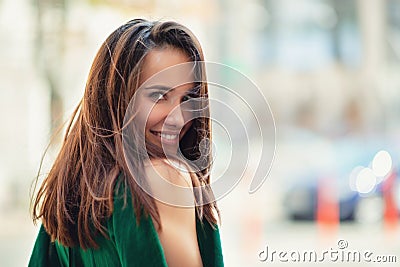 Young pretty likable cheerful woman posing summer city outdoor. Beautiful self-confident girl dressed in emerald-colored jumpsuit Stock Photo