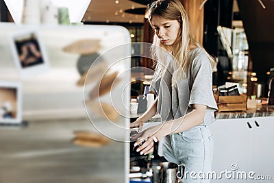 A young pretty thin blonde,dressed in casual outfit,is cooking coffee in a popular coffee shop. Stock Photo