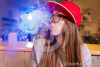 Young pretty woman in red cap smoke an electronic cigarette at the vape shop Stock Photo