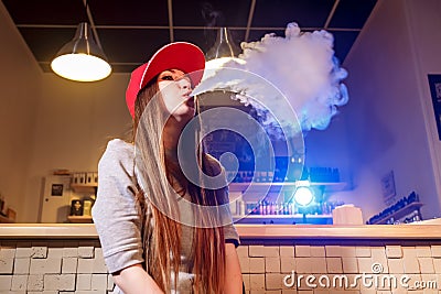 Young pretty woman in red cap smoke an electronic cigarette at the vape shop Stock Photo