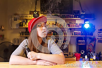 Young pretty woman in red cap smoke an electronic cigarette at the vape shop Stock Photo