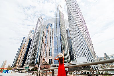 Young pretty woman in red dress and straw hat pointed with hands on downtown skycrapers in modern city. Low angle view Editorial Stock Photo