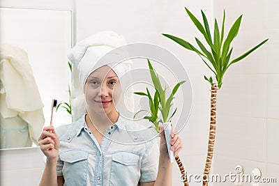 A young pretty woman with a towel on her head in a bright bathroom with a toothbrush and paste in her hands Stock Photo