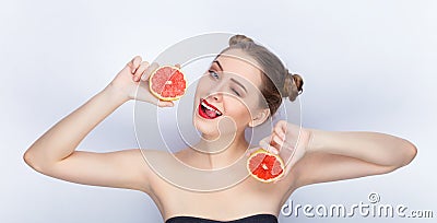 Young pretty woman trendy makeup bright red lips bun hairstyle bare shoulders act the ape with grapefruits white studio background Stock Photo