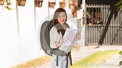 Young pretty woman wearing casual clothing and backpack standing in front of camera, smiling happily, holding map Stock Photo