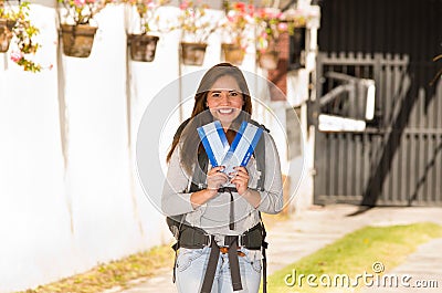 Young pretty woman wearing casual clothing and backpack standing in front of camera, smiling happily, holding travel Stock Photo