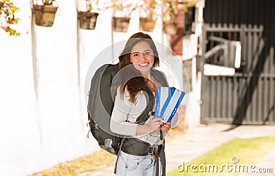 Young pretty woman wearing casual clothing and backpack standing in front of camera, smiling happily, holding travel Stock Photo