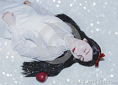 Young pretty woman with white skin and red lips is lying on the snow with red poisoned apple.Snow white princess Stock Photo