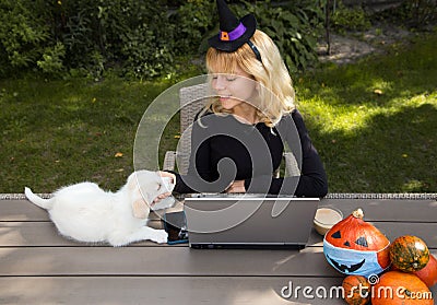Young pretty woman in witch hat. Sits at table in garden, works at laptop Stock Photo