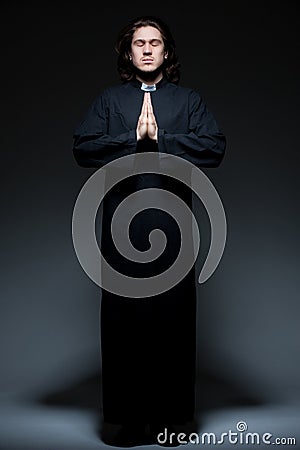 Young priest is praying against dark background Stock Photo