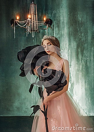 The young princess embraces fabulous, huge, black roses in the Gothic style. The girl has a crown and a luxurious, lush Stock Photo