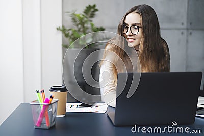 Young professional doing creative project on laptop. Girl sitting by computer at office desk. Digital tools and solutions for Stock Photo
