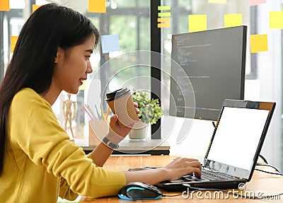 Young professional woman uses a laptop for work and online meetings, she holds a coffee cup and works from home Stock Photo