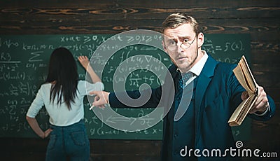 Young professor pointing at the board while holding book in straight hand. Young teacher giving explanations to students Stock Photo