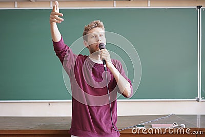 Young professor teacher speaking with the microphone in the lecture hall standing near blackboard Stock Photo