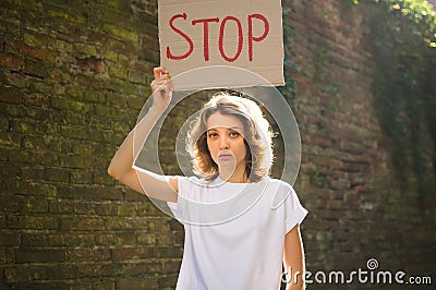 Young protesting woman in white shirt and jeans holds protest sign broadsheet placard with slogan `Stop` for public Stock Photo