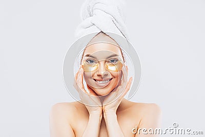 Young pure beautiful gentle woman with a towel on head standing naked isolated looking camera take care of her skin with under eye Stock Photo