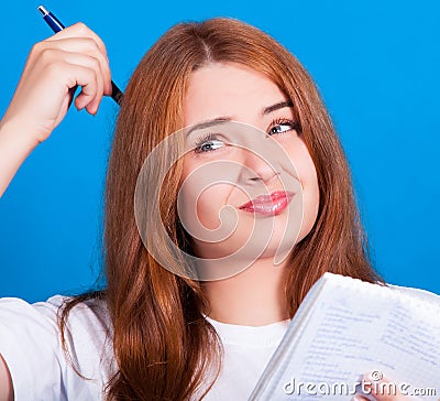 Young red-haired girl with blue eyes in a white t-shirt thinks what to write in a notebook. Stock Photo